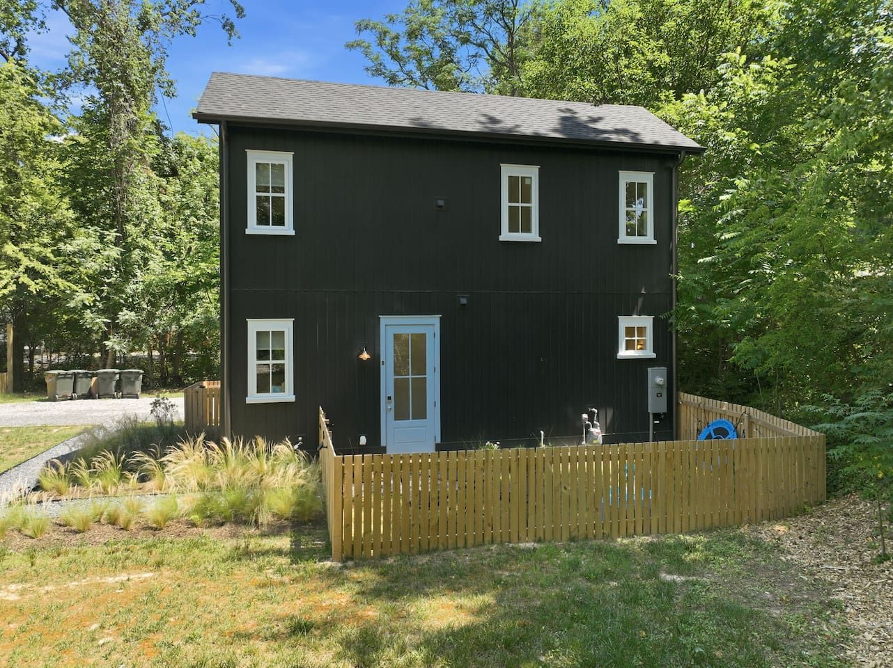 Une maison à deux étages, à l’extérieur sombre, avec une porte blanche et une cour clôturée.