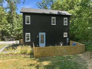 Uma casa de dois andares com fachada escura, porta branca e quintal cercado.