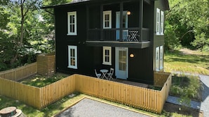 A two-story black building with a balcony, a door labeled '700 A', and a small outdoor seating area with two chairs. - Downtown Centric, Tucked Away, Fenced, PetsOK (Durham)