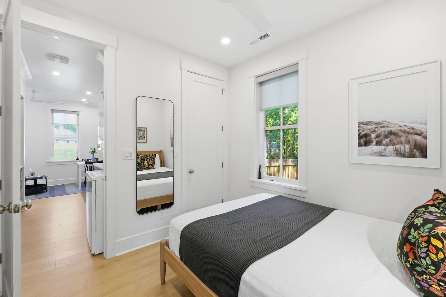 A bedroom with a bed, a window, a mirror, and a door leading to a bathroom.