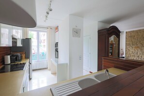 Eine Küche mit Herd, Wasserkocher und Kühlschrank. Ein Fenster bietet Blick auf einen Balkon.