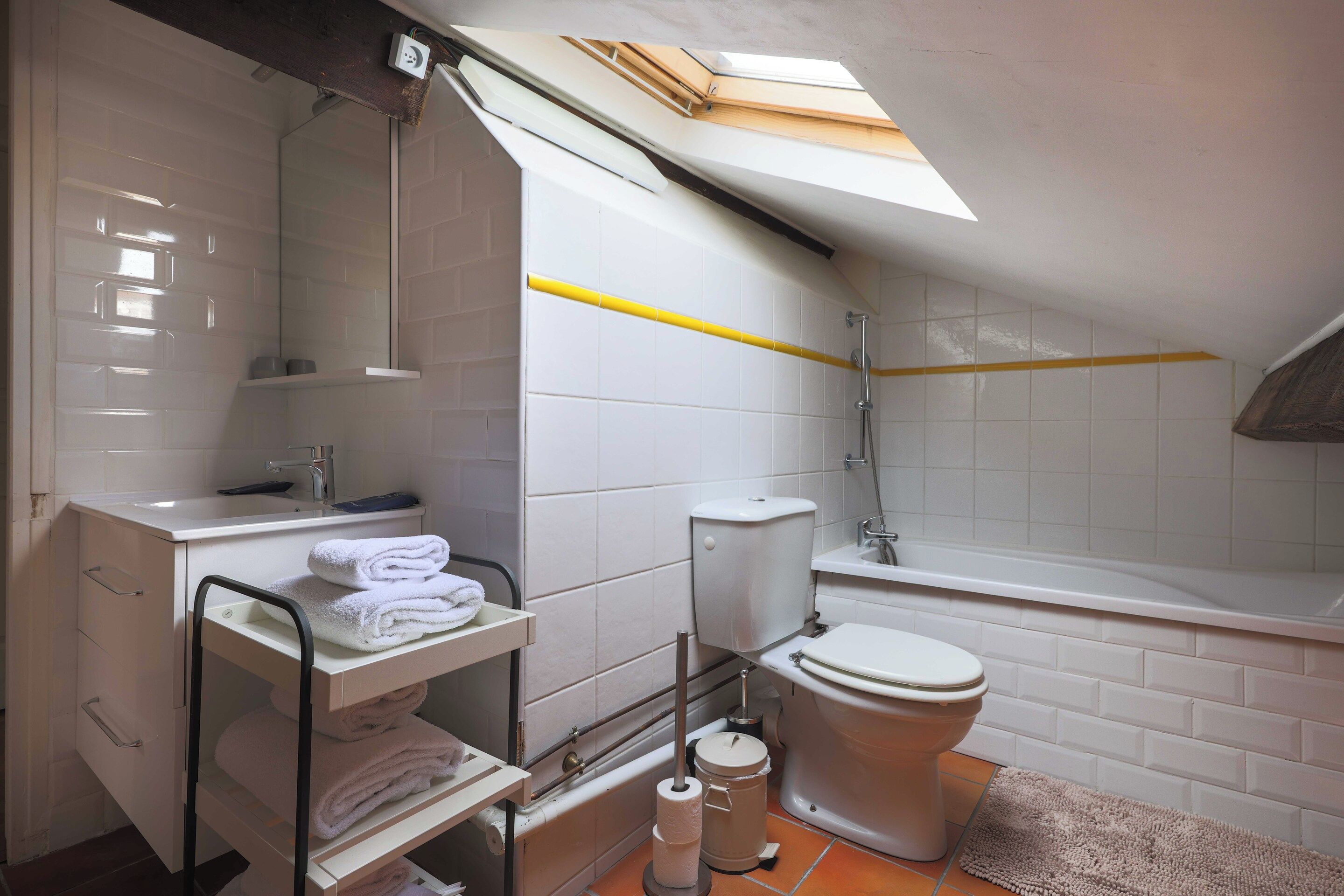 Ein modernes Badezimmer mit Oberlicht, weißen Fliesen, Toilette, Waschbecken und Dusche.