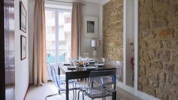 A dining area with a table set for four, clear chairs, a stone wall, and a balcony with a view.
