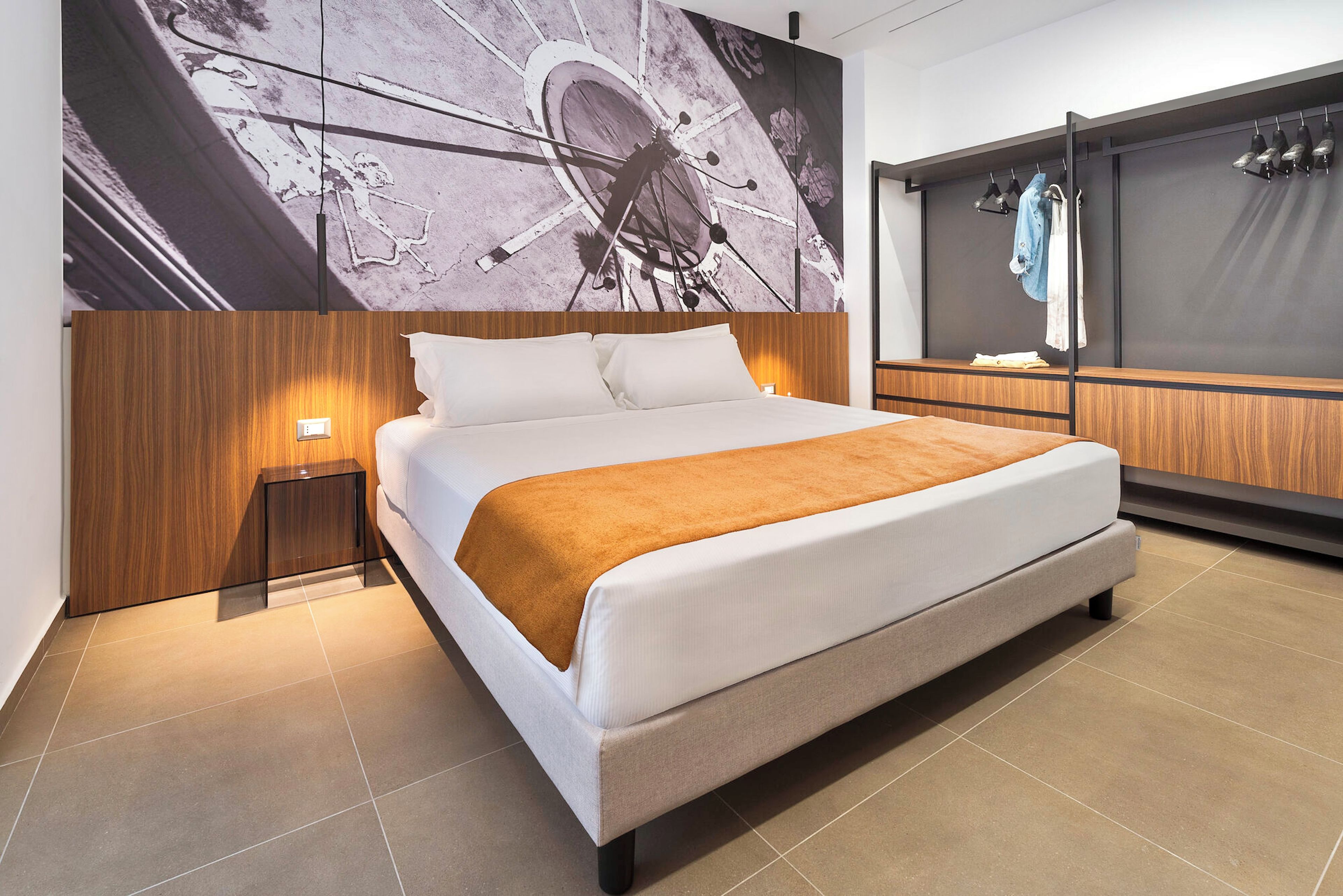 A modern hotel room with a large bed, a nightstand, a wooden headboard, and a wall-mounted TV.