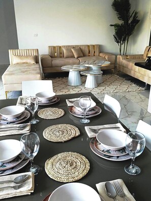 Un comedor con una mesa negra dispuesta para una comida, rodeado de sofás y una mesa de centro.