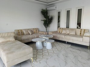 A modern living room with a beige sectional sofa, a coffee table, and a potted plant. - Escape to Villa Yasmina (Aghir)