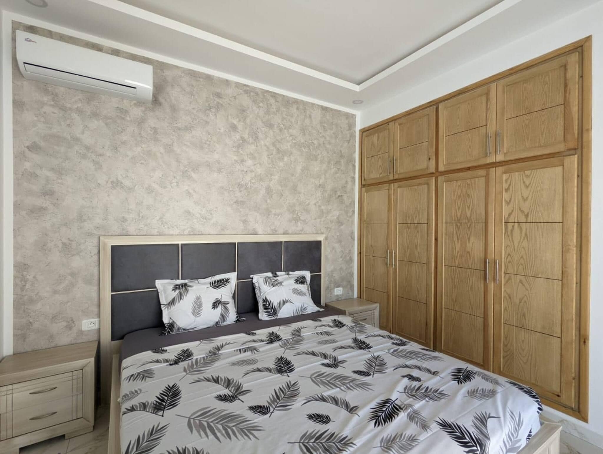 Un dormitorio con cama, mesitas de noche, aire acondicionado y armario de madera.