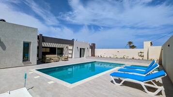 Un área de piscina moderna al aire libre con un cielo azul despejado, una piscina y sillas de descanso.
