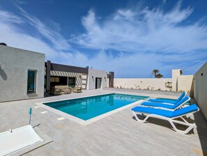 A modern outdoor pool area with a clear blue sky, a pool, and lounge chairs. - Escape to Villa Yasmina (Aghir)