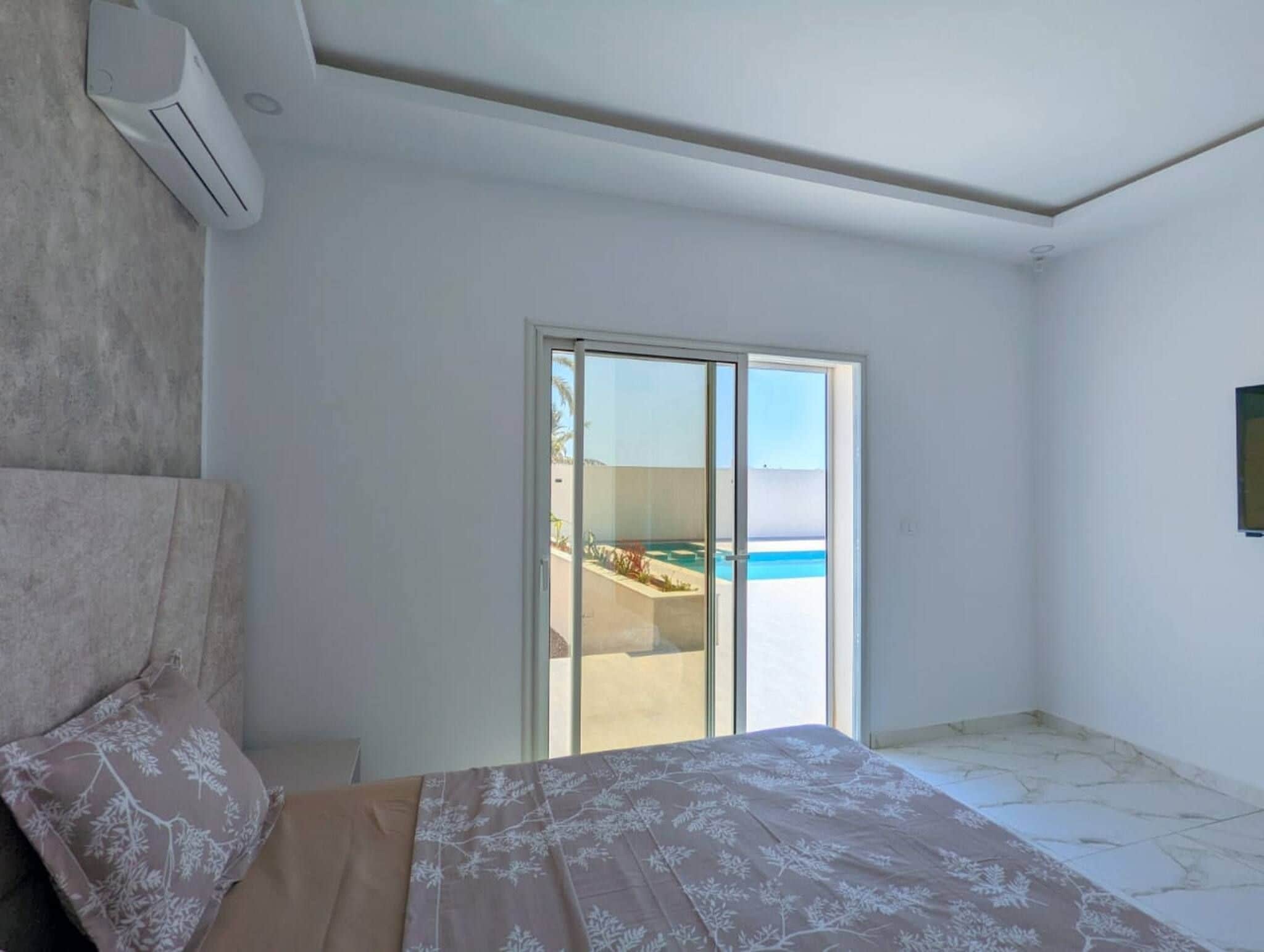 Un dormitorio con cama, puerta corrediza de vidrio a un balcón y vista al océano.