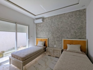 Un dormitorio moderno con dos camas, un ventanal grande y una pared de concreto.