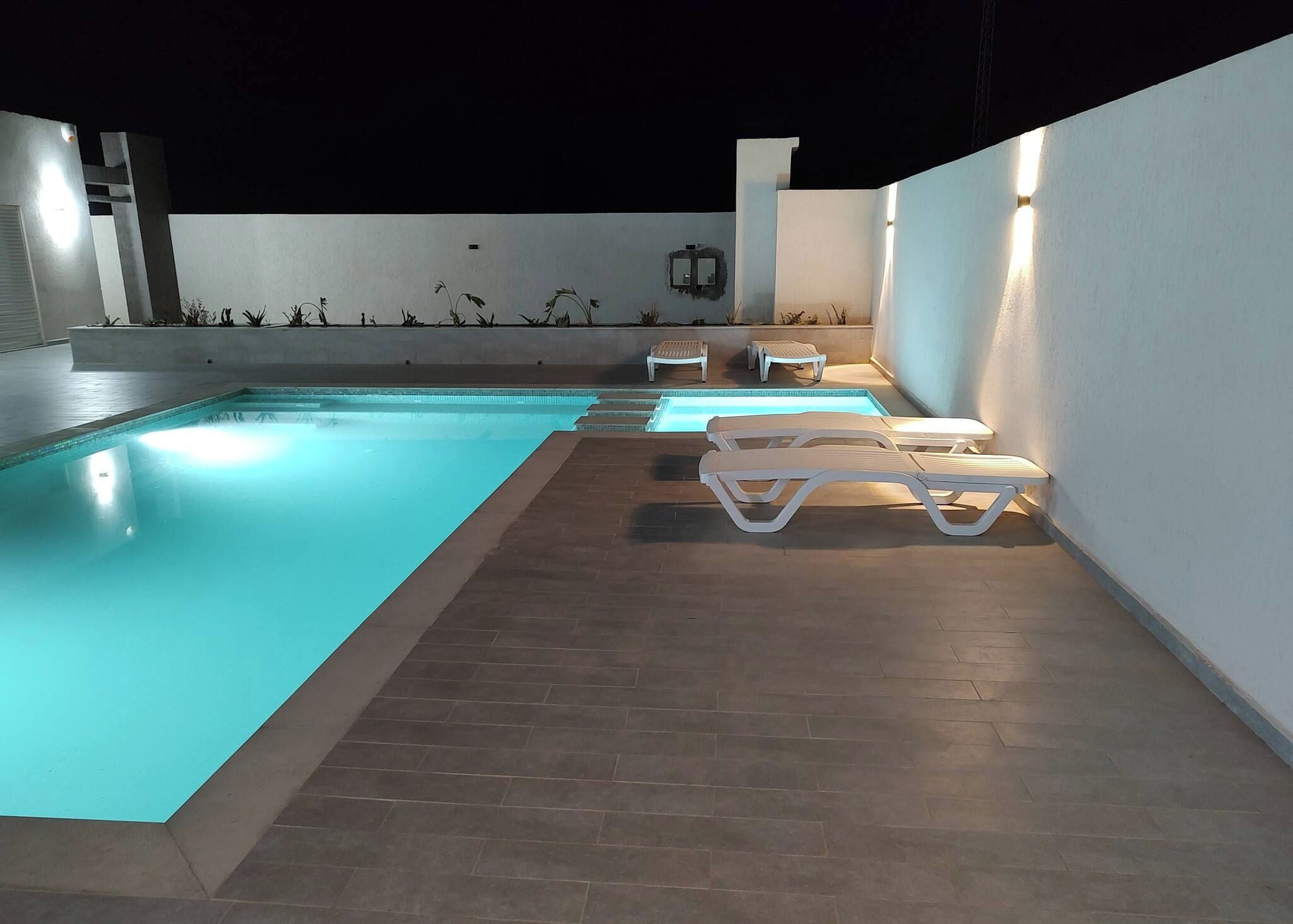 An outdoor swimming pool with a tiled deck and white lounge chairs.