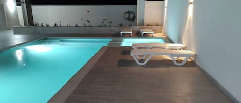 An outdoor swimming pool with a tiled deck and white lounge chairs.