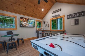 A room with a pool table, a television displaying a scenic outdoor view, and a sign indicating a game room. - Sauna-Hot tub-Pool table-Pickleball-Treehouse with slide-Golf putting green (Blue Ridge)