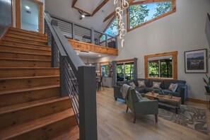 A spacious living area with a wooden staircase, a loft bedroom, and large windows offering views of the outdoors. - Sauna-Hot tub-Pool table-Pickleball-Treehouse with slide-Golf putting green (Blue Ridge)