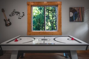 Een tafelvoetbaltafel met erboven een raam, een gitaar, en een muur met muzieknoten en een schilderij.