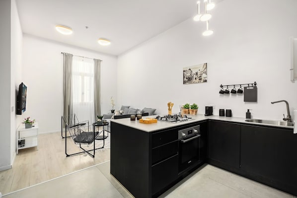 A modern kitchen with black cabinetry, a central island, and a dining area with a chair and table. - The Monti – Stylish 1‑Bedroom Apartment in Central Tel Aviv (Tel Aviv-Yafo)