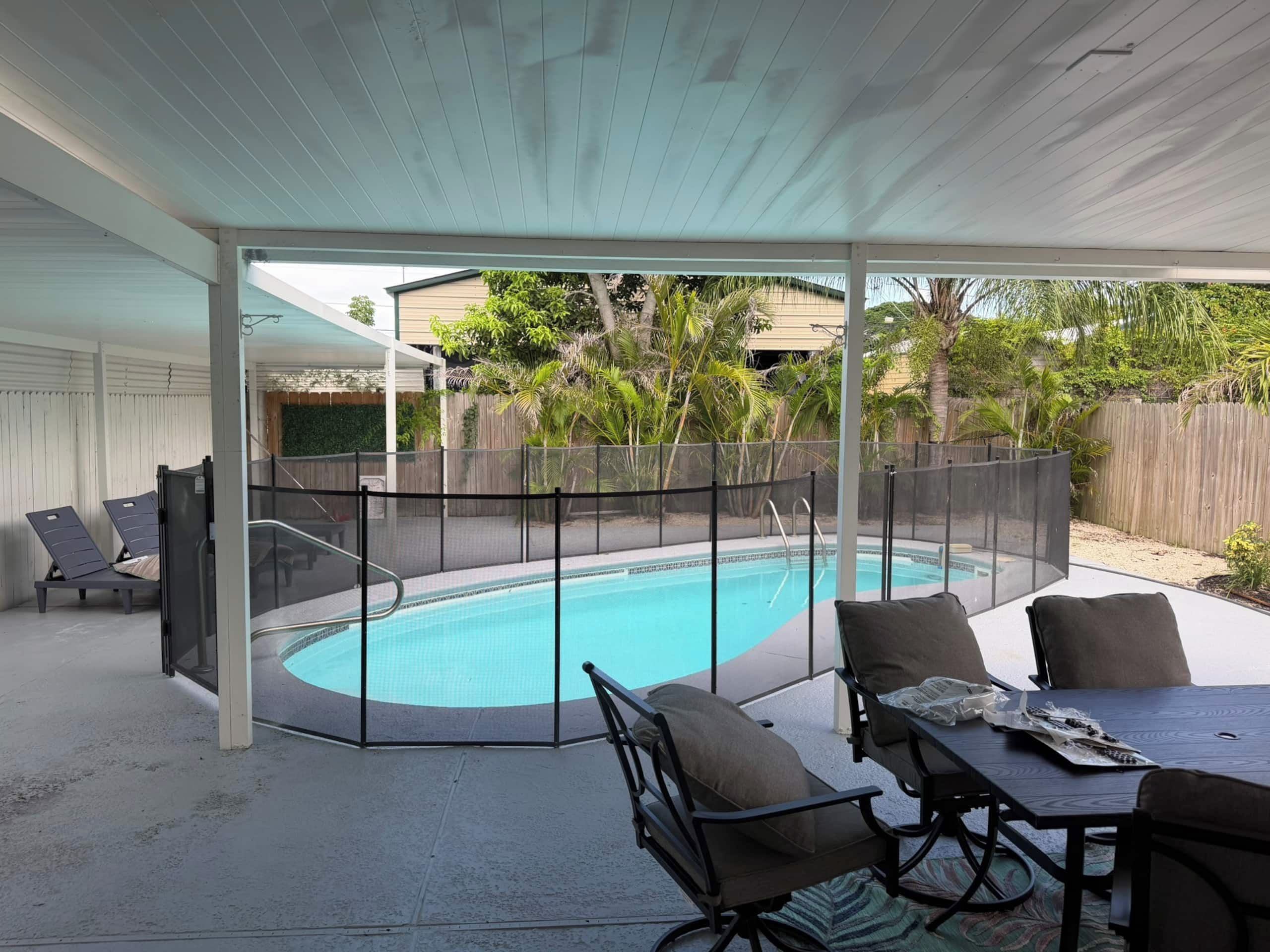 A covered outdoor area with a pool, seating, and a fenced enclosure.