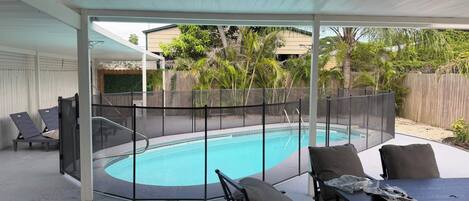 A covered outdoor area with a pool, seating, and a fenced enclosure.