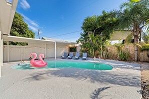 Ein Swimmingpool mit zwei Flamingo-Schwimmdschaumen, umgeben von Liegestühlen und einem Holzzaun.