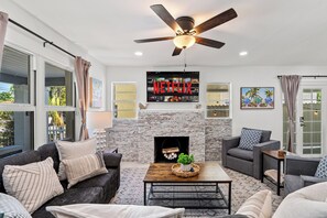 A living room with a fireplace, a ceiling fan, and a mounted TV displaying the Netflix logo. - West Palm Pool Home Sleeps 10 Game Room (West Palm Beach)