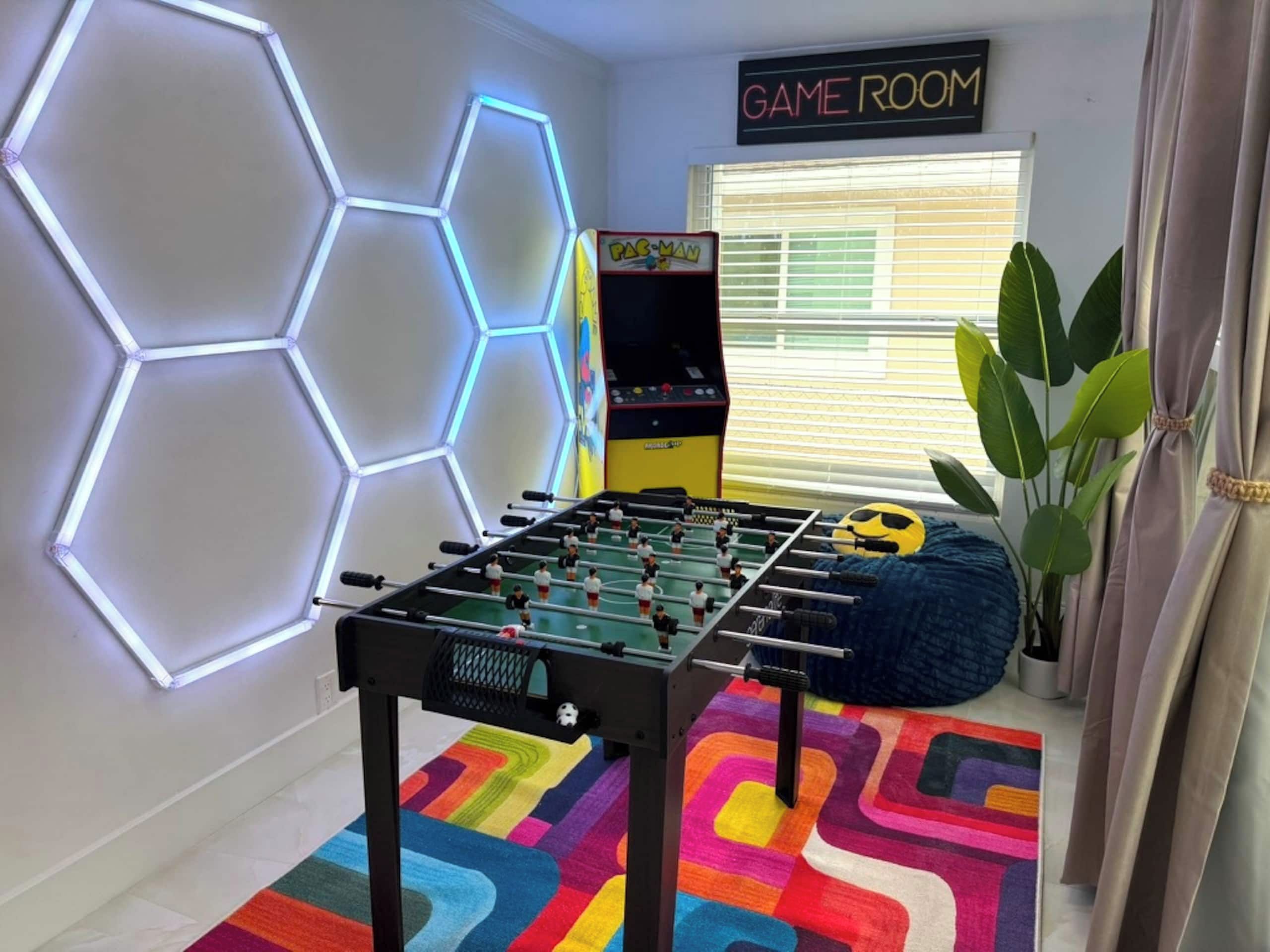 A room with a foosball table, a Game Room sign, a hexagonal light fixture, and a colorful rug.