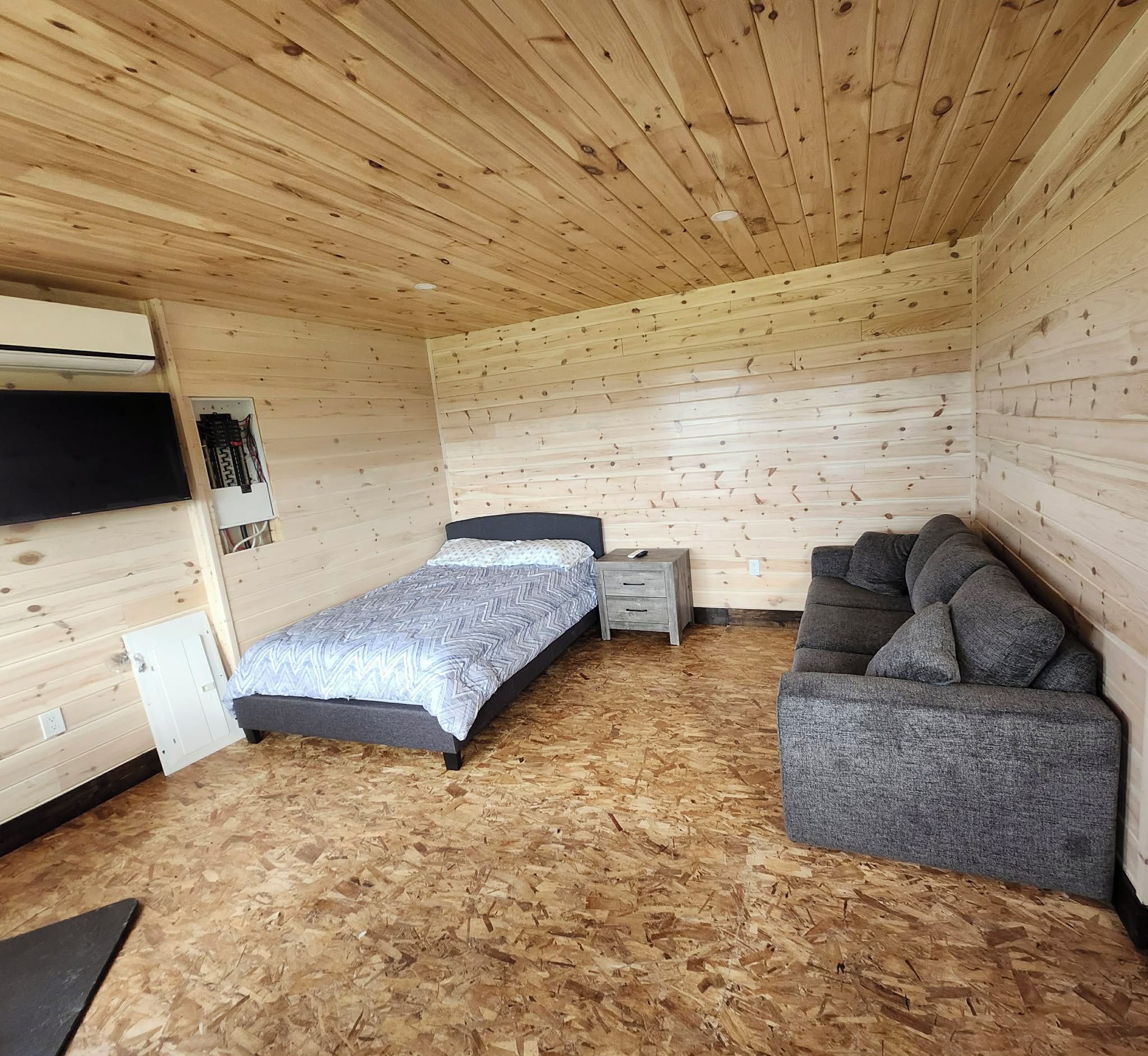 Ein gemütlicher Raum mit einem Bett, einem grauen Schlafsofa und einem kleinen Nachttisch.