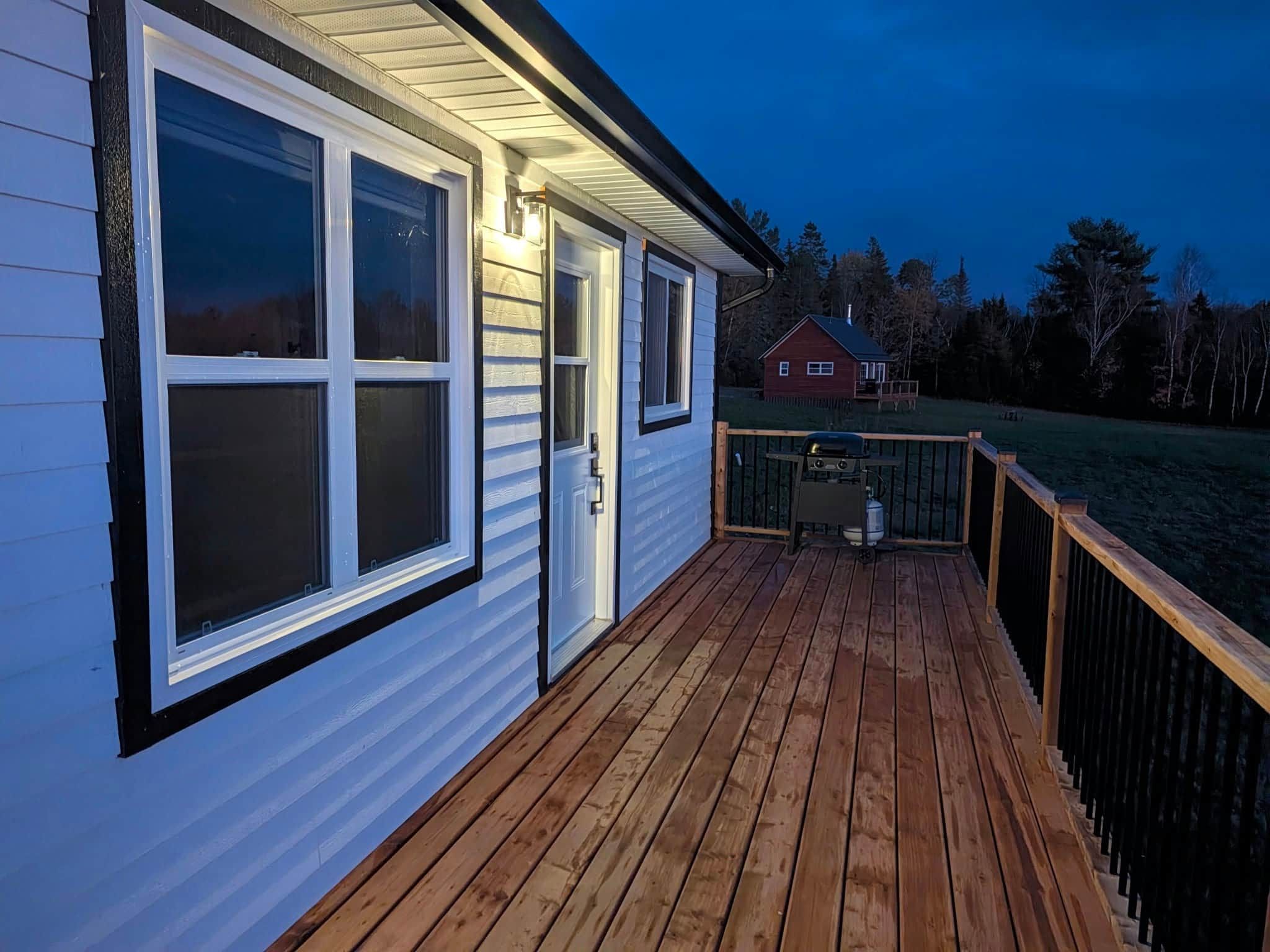 Eine Holzterrasse mit Geländer, ein Haus mit weißer Fassade und rotem Dach, und ein klarer Himmel.