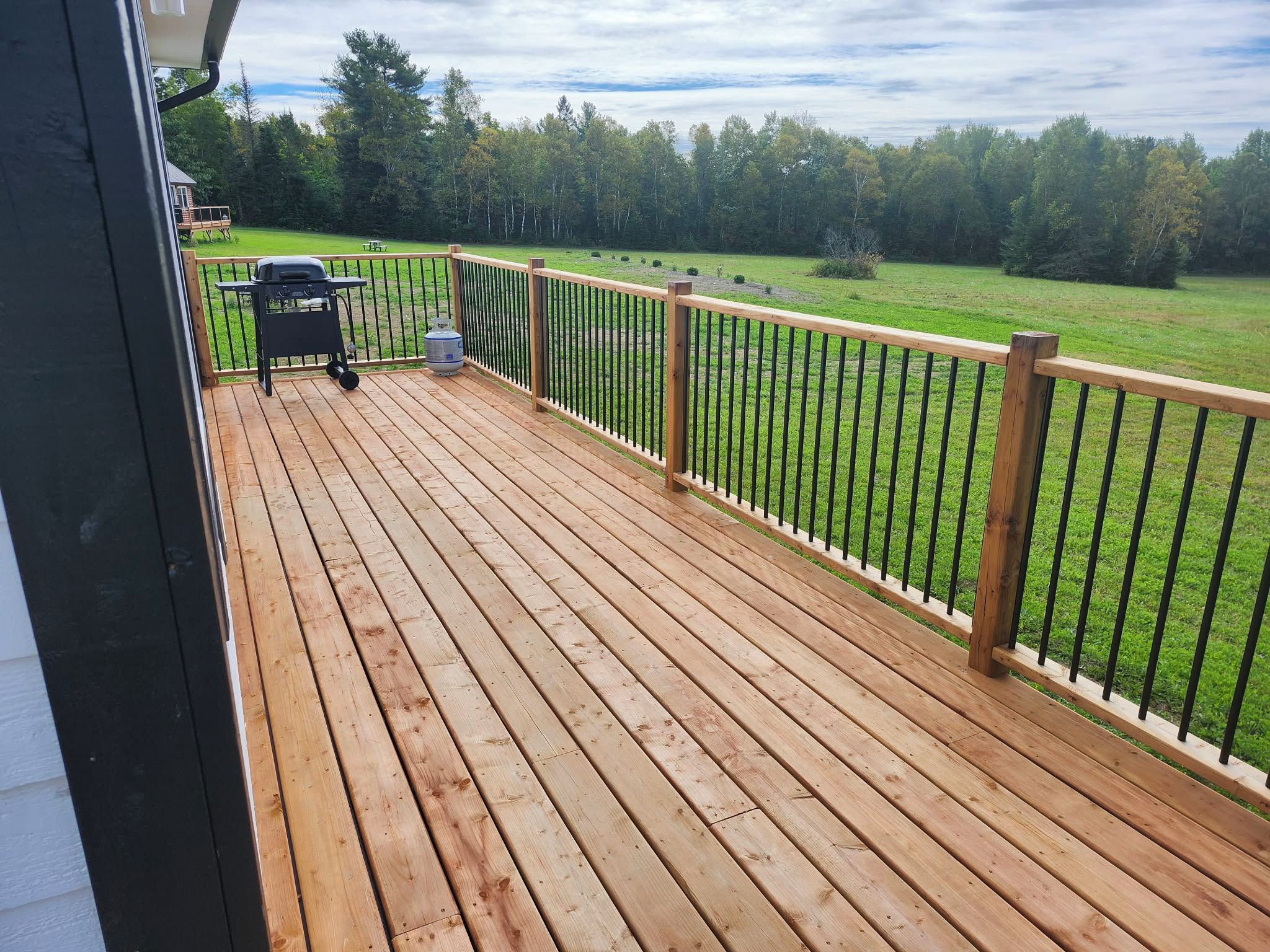 A wooden deck with a metal railing, a grill, and a propane tank.