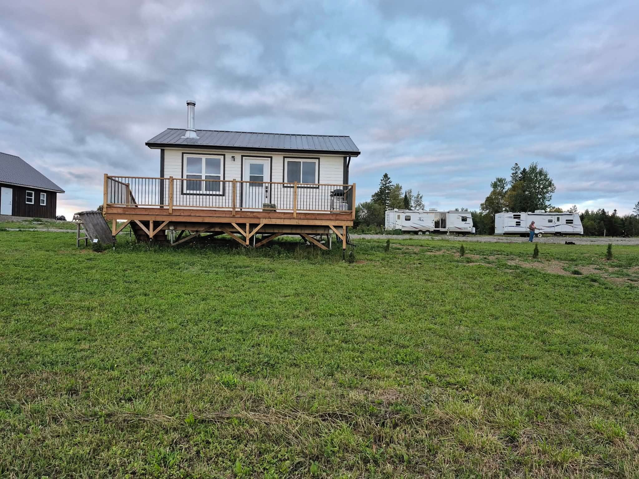 A single-story house with a deck, surrounded by a grassy field and trees.