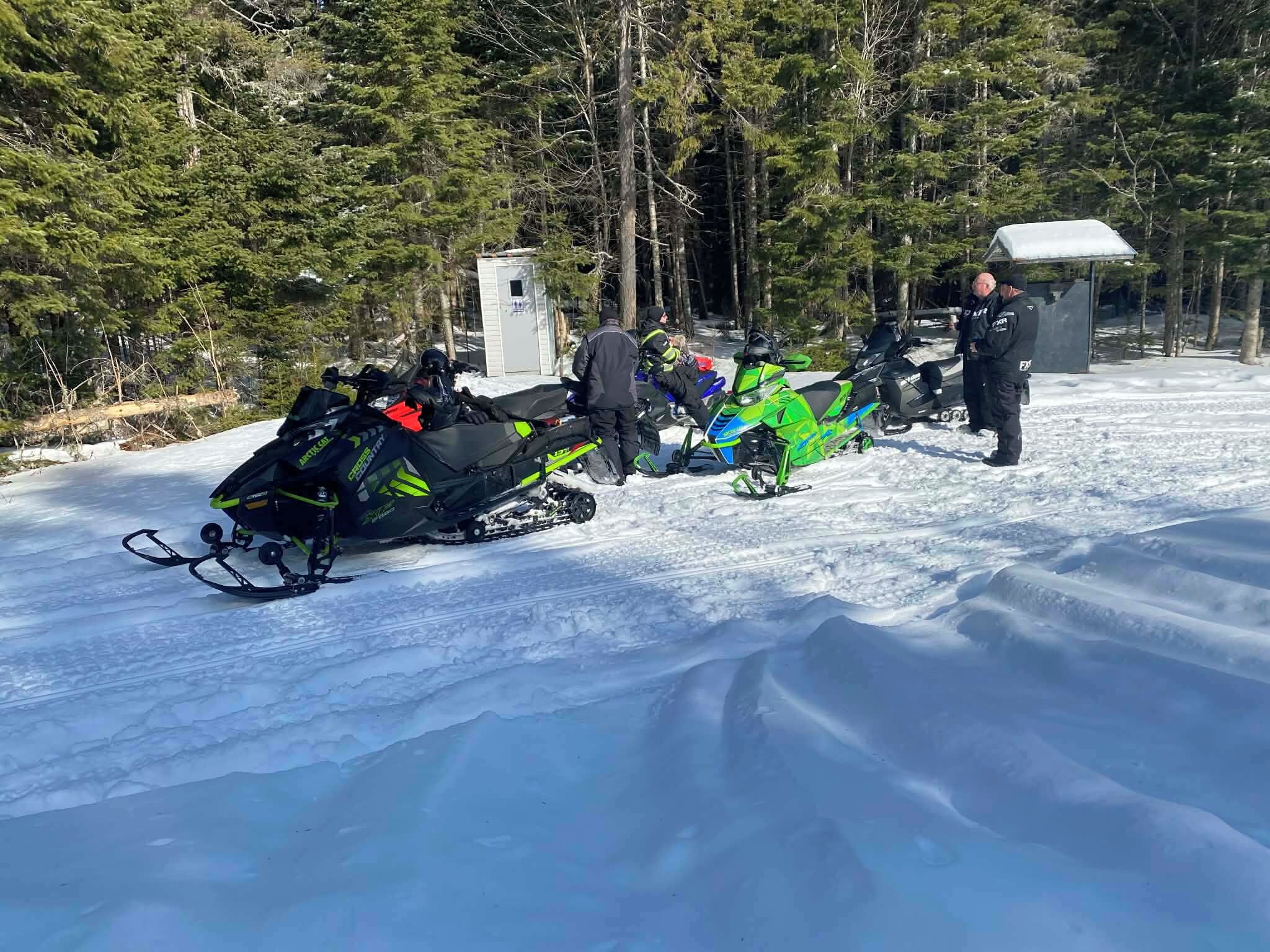 A snowy landscape with snowmobiles and a small building.