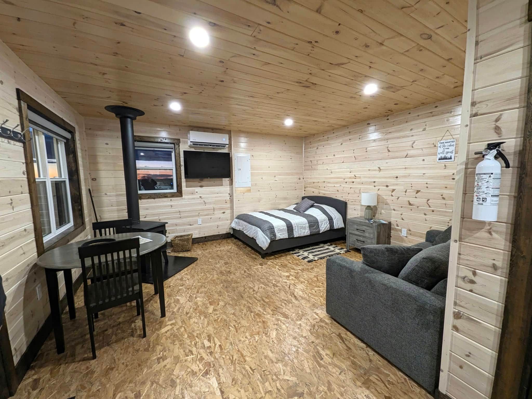 Ein gemütliches Blockhaus mit einem Bett, einer Couch, einem Tisch mit Stühlen, einem Fernseher und einem Kamin.