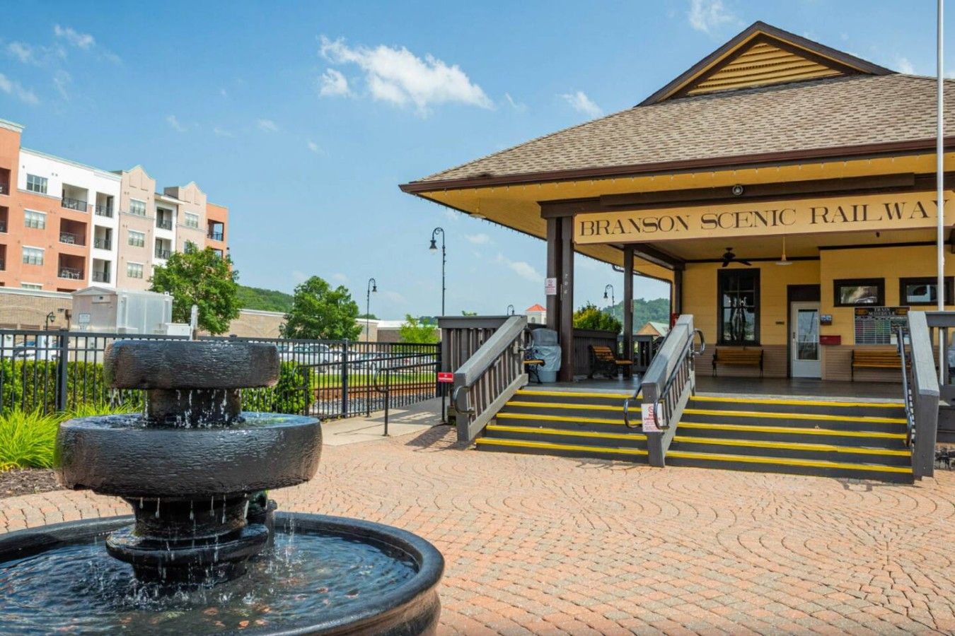 A Branson Scenic Railway station with a fountain, steps, and a covered waiting area.