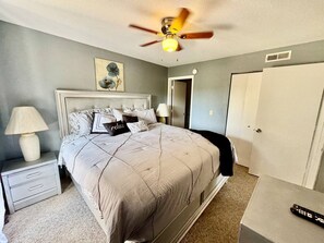A bedroom with a bed, nightstands, a ceiling fan, a door, and a remote control on a table. - SDC Ground Level Condo (Branson)