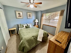 Ein Schlafzimmer mit einem Bett, einem Nachttisch, einer Lampe, einer Holzkommode und einem Deckenventilator.