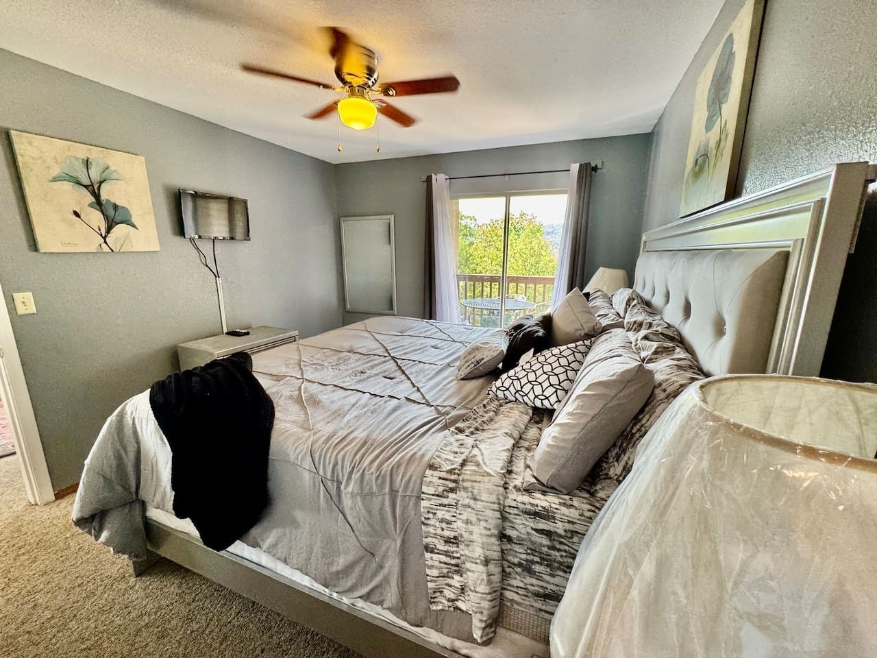 A bedroom with a bed, a ceiling fan, a window with curtains, and a painting on the wall.