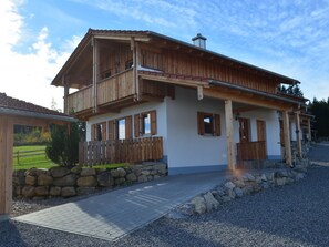 A two-story wooden house with a balcony, stone wall, and a gravel driveway. - Holiday Home With 3 Bedrooms (Lechbruck)