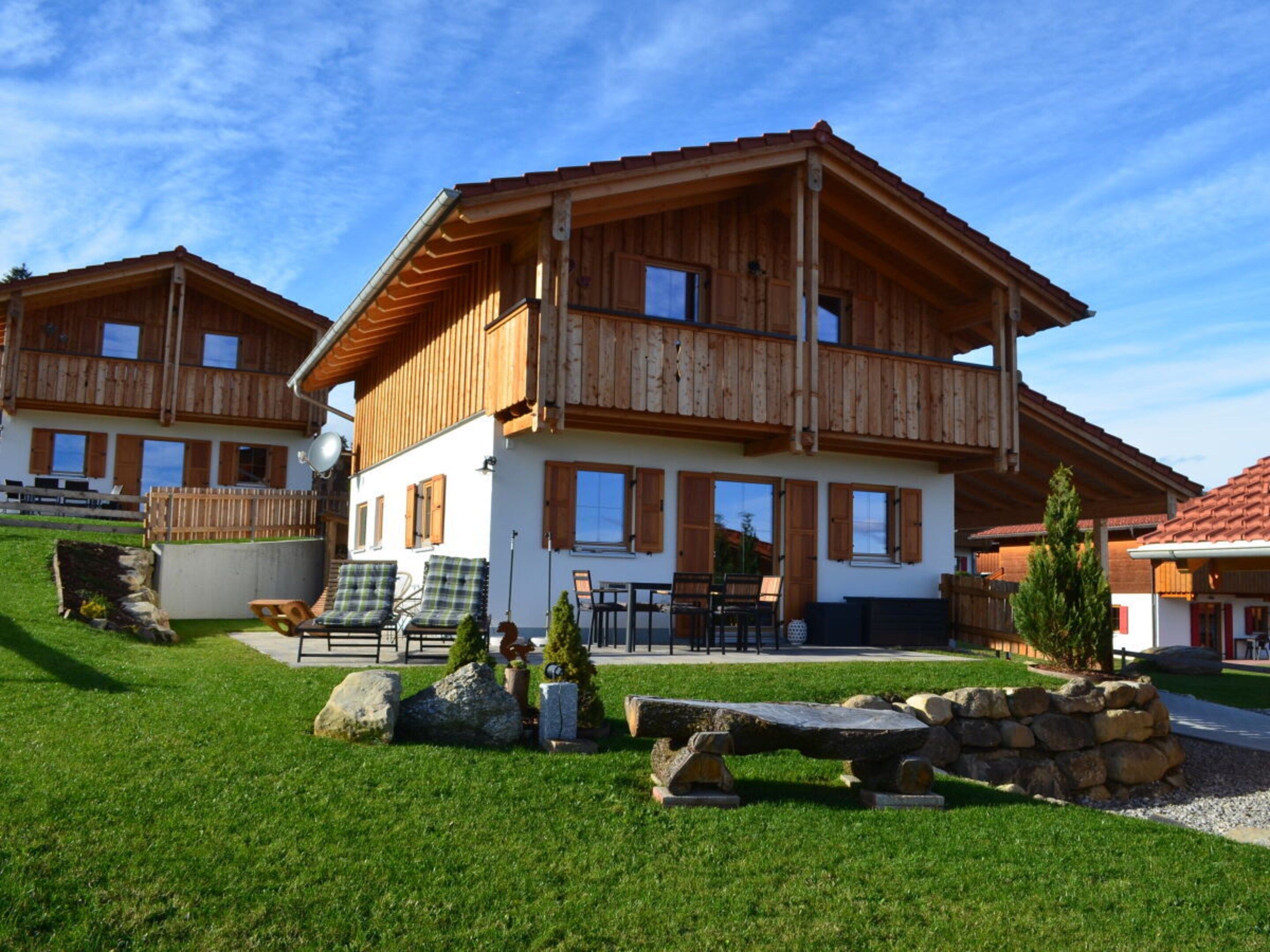 A two-story wooden chalet with a balcony, outdoor seating, and a well-maintained lawn.