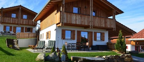 Un chalet de madera de dos pisos con un balcón, mobiliario exterior y un césped bien cuidado.