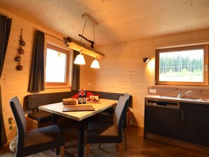 A cozy cabin-style kitchen with a wooden table and chairs, a built-in oven, and a window with a view of the forest. - Holiday Home With 3 Bedrooms (Lechbruck)