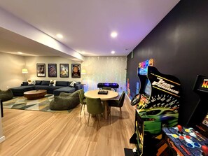 Un salon moderne comprenant un ensemble de canapés, une table basse, une table à manger avec des chaises et un espace de jeux équipé d’une console de jeux de course.