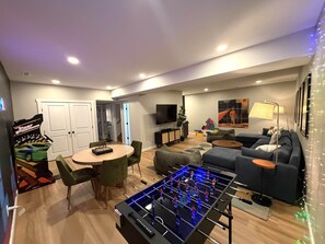 A modern living room with a foosball table, a sofa, a TV, and a dining area with chairs. - Eagle's Landing Chalet (Massanutten)
