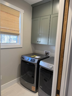 A laundry room with two front-loading washing machines, a window with blinds, and a door leading to another room. - Eagle's Landing Chalet (Massanutten)