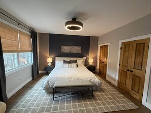 A bedroom with a bed, bedside tables, a ceiling light, a window with curtains, and a door. - Eagle's Landing Chalet (Massanutten)