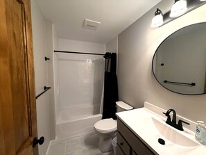 Une salle de bain avec des toilettes blanches, une baignoire, une douche, un lavabo avec un miroir et une porte.
