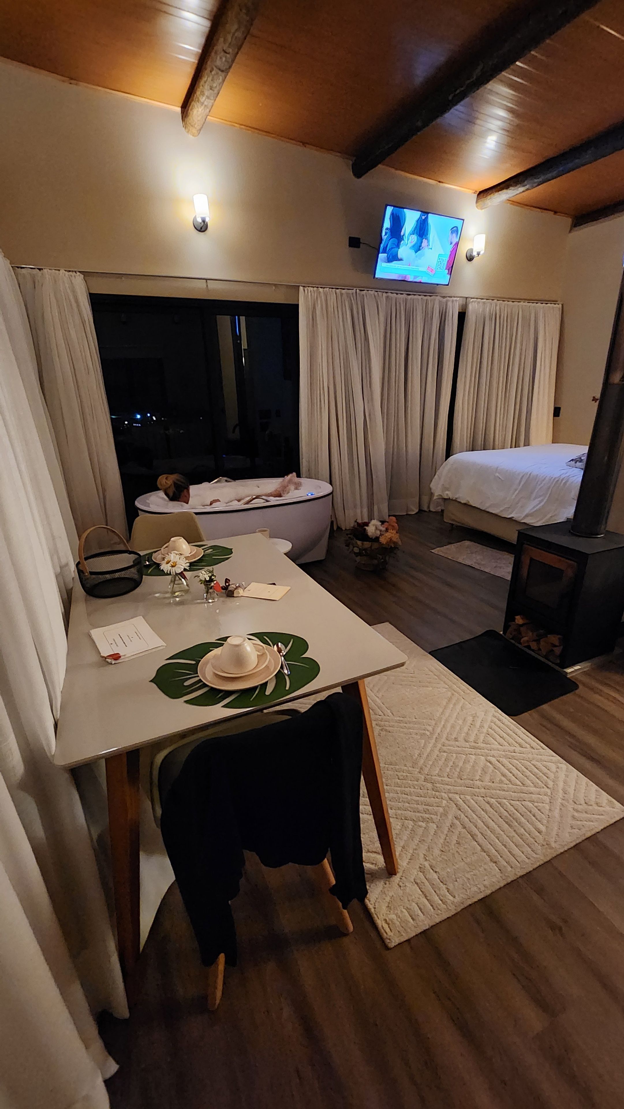 Quarto acolhedor com cama, mesa posta para refeições, televisão e lareira.