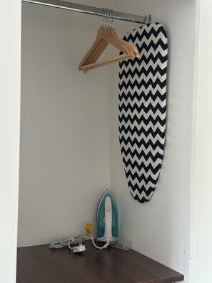 A room with a wooden hanger, a black and white zigzag patterned item, a teal iron, and a white cable.