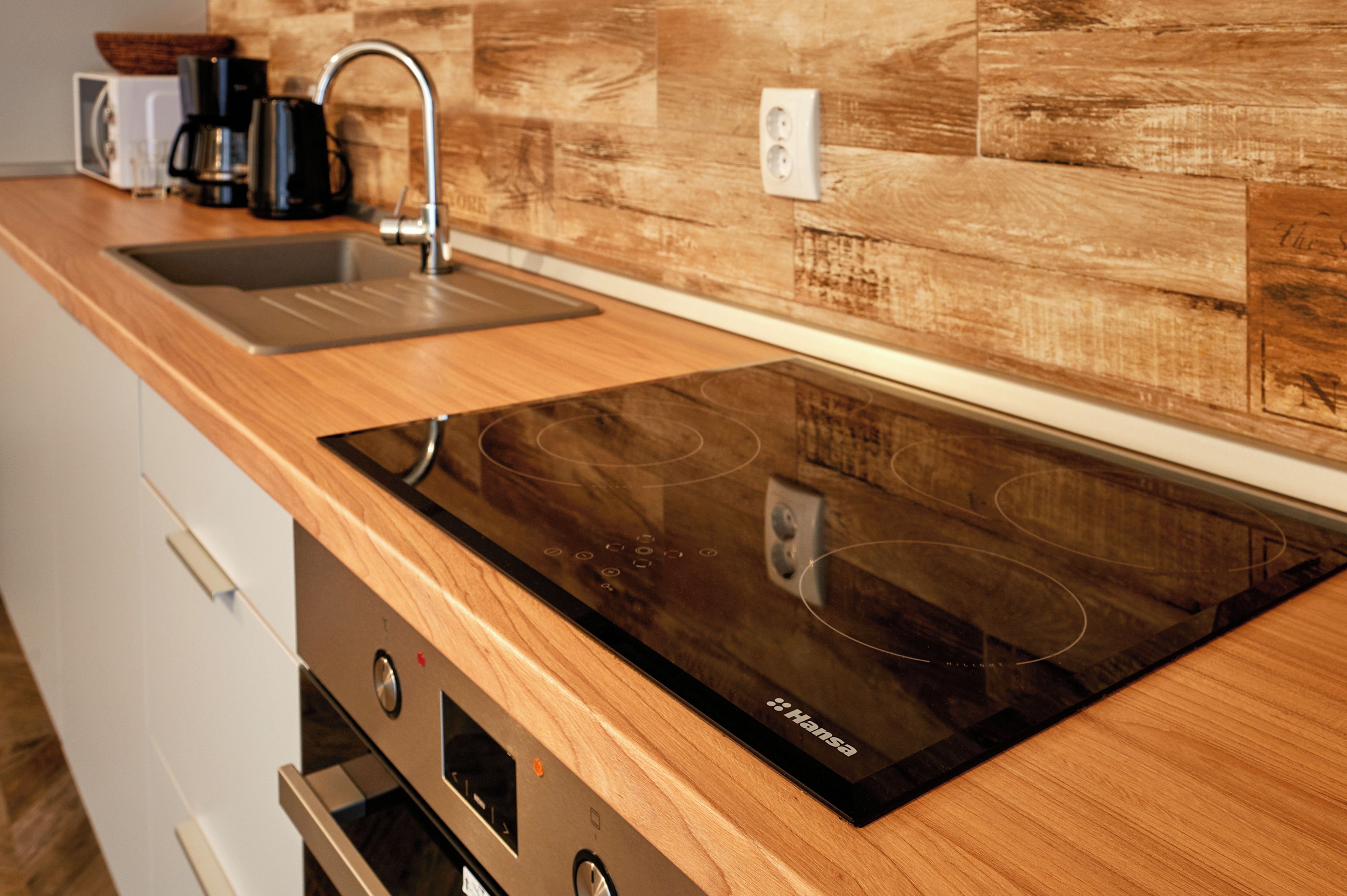 Una cocina con encimera de madera, placa de inducción negra, pileta de acero inoxidable y cafetera.