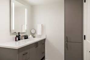 Un bagno moderno con un mobile bagno bianco, un grande specchio, uno specchio tondo e un portasciugamani.