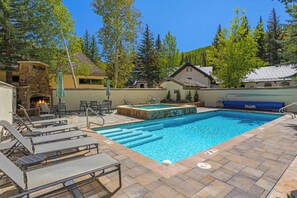 A swimming pool with lounge chairs and a stone fireplace. - Villa Cortina 135 | 2BR Vail Village Retreat with Pool (Vail)